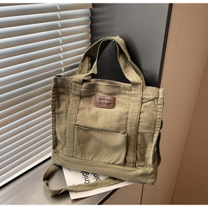 Close-up of army green canvas tote bag featuring a leather patch and front square pocket
