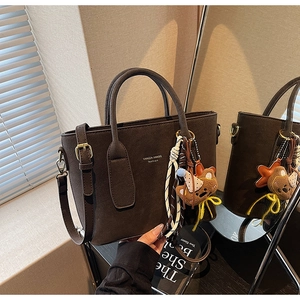 Détail d'un sac bandoulière en daim mat marron foncé avec breloque ours et sangle