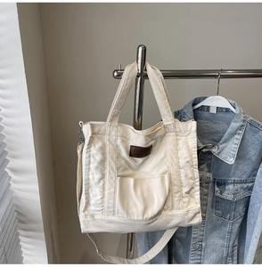 Detail of off-white canvas tote bag with brown leather patch and denim jacket setting