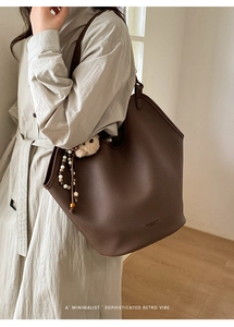 Détail d'un grand sac cabas en cuir marron foncé avec un pendentif ours et des perles