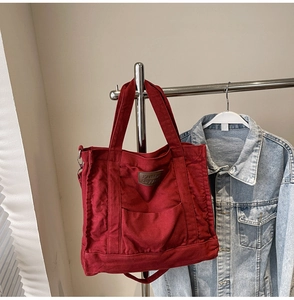 Detail of red canvas tote bag with front pocket, metal ring, and fashion luggage label