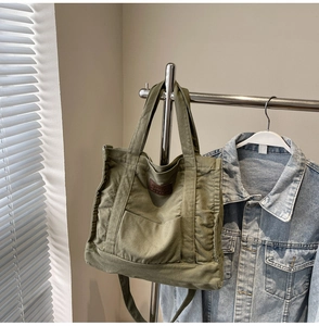 Detail of olive green canvas tote bag with brown leather patch and dual strap design