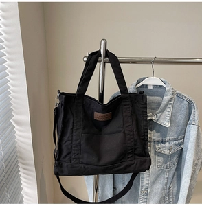 Detail of black canvas tote bag with leather logo patch and adjustable crossbody strap