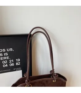 Détail de la fine bandoulière nouée et de la boucle en métal doré sur le sac en daim brun