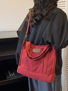 Large red canvas tote bag with shoulder strap shown worn by a model in casual style