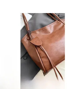 Detail of brown leather tote bag showing tassel charm and knotted handle texture