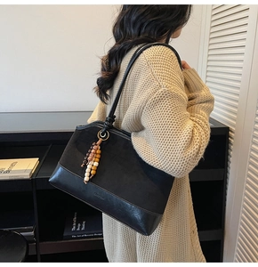 Dettaglio della borsa shopper nera con ciondolo di perline e tracolla sulla modella