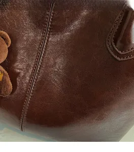 Detail view of smooth brown vintage leather texture and plush bear charm on tote bag