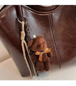 Close-up of a brown teddy bear pendant with a LOVE ribbon on a lychee-textured leather tote