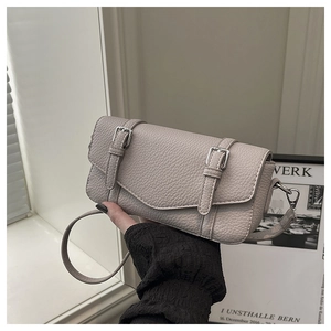 Primer plano de bolso en cuero beige texturizado con hebillas plateadas y correa fina