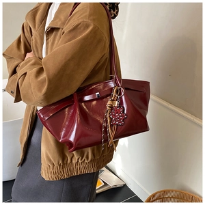 Detail of burgundy glossy tote bag with decorative buckle and leopard bear charm