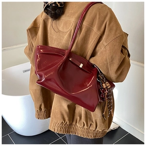 Detail of burgundy patent leather tote bag with bow strap and beaded charm on model