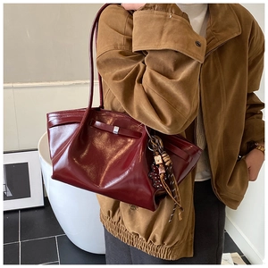 Deep red patent leather tote bag with glossy finish and tassels on a female shoulder