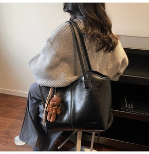 Detail of black glossy leather tote bag with long straps and a brown plush bear charm