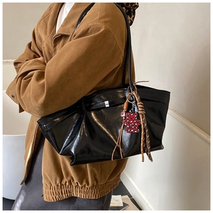Close-up of black leather tote bag featuring buckle straps and leopard heart charm