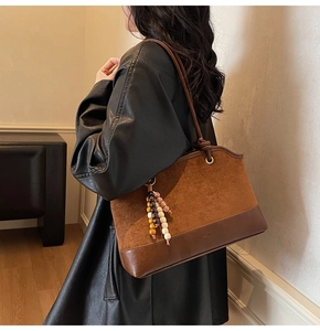 Dettaglio di patchwork in pelle scamosciata marrone e ciondolo di perle sulla borsa