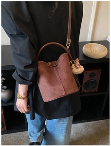Detailansicht einer braunen Wildleder-Beuteltasche mit Bärenanhänger im Lifestyle-Stil