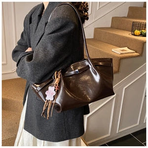 Close-up of a glossy dark brown leather tote bag featuring a purple bear charm and metal buckle