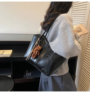 Detail of black oil-wax leather tote bag with plush bear charm and thin shoulder straps