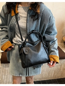 Detailed view of black faux leather tote featuring decorative round buckle and tassel