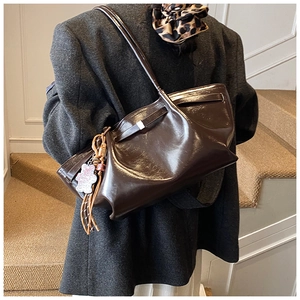 Detail of dark brown glossy tote bag featuring floral charm and stylish long tassels