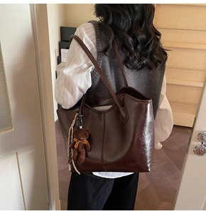 Detail of a large dark brown faux leather tote bag with a cute plush bear charm