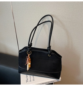 Dettaglio della borsa tote in pelle scamosciata nera con ciondolo etnico e logo inciso