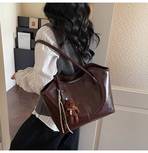 Detail of dark brown glossy leather tote bag with bear charm and woven tassel detail