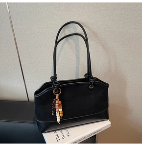 Dettaglio della borsa tote nera con mix di texture, ciondolo in legno e oggetti quotidiani