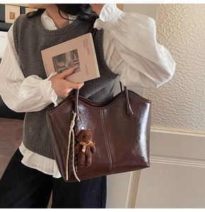 Detail of dark brown glossy tote bag with cute bear charm and vertical stitching texture