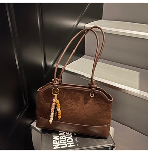Dettaglio di borsa tote marrone scuro con texture scamosciata e ciondolo a nappa con perline