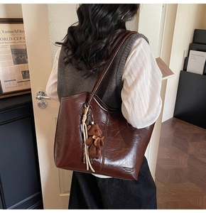 Detail of dark brown glossy tote bag with cute bear charm and woven tassel detail