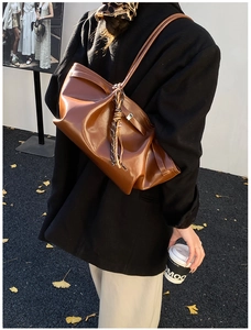 Detailed view of brown leather tote bag with stylish striped scarf and autumn leaves