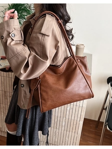 Detail view of large brown faux leather tote with shoulder straps and tassel charm