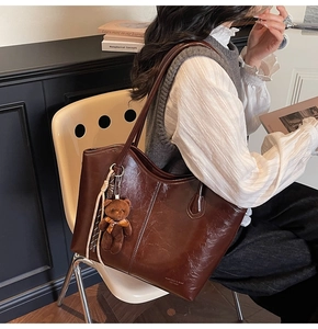 Detail of dark brown leather tote bag with bear charm worn on shoulder by a model