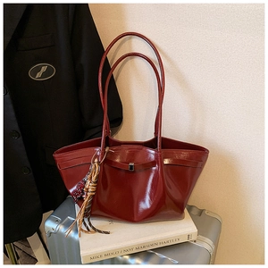 Close-up of a glossy burgundy tote bag with tassel detail and sleek shoulder straps