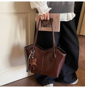 Detail of dark brown glossy leather tote bag with a plush bear charm for daily commute