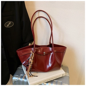 Detail of burgundy glossy tote bag featuring slim shoulder straps and woven tassel charm