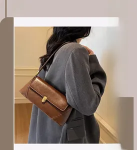 Detail of vintage brown leather underarm bag with gold flap lock on tweed coat