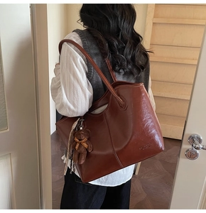 Detail view of large brown leather tote bag with vintage finish and cute bear charm