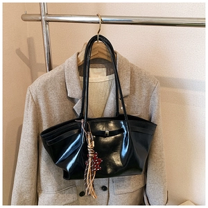 Detail of glossy black tote bag with silver buckle and leopard tassel on grey suit backdrop
