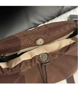 Detail shot of a dark brown checkered nylon backpack with a metal magnetic snap closure