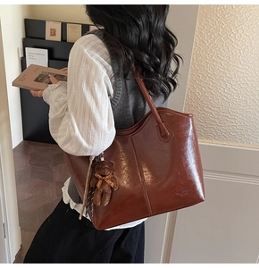 Close-up of a brown PU leather tote bag featuring vertical stitching and a plush bear charm