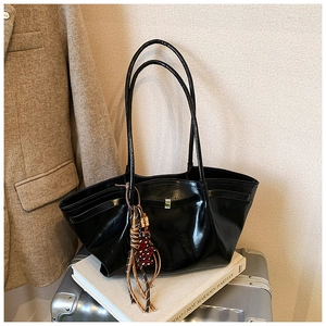 Close-up of a black glossy tote bag with a colorful tassel on a silver suitcase