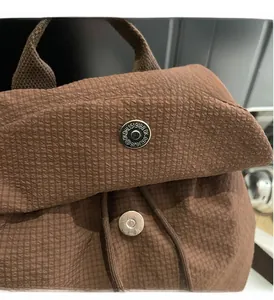 Close-up of brown textured nylon backpack with silver magnetic buckle and drawstring detail