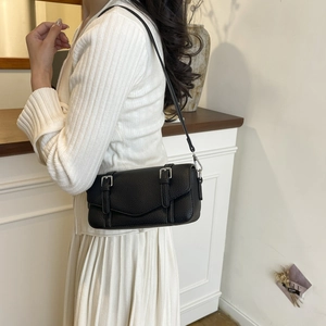 Detalle de bolso bandolera negro con textura litchi y hebillas plateadas en jersey
