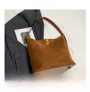 Close-up of brown suede tote bag featuring a gold metal twist-lock and leather straps
