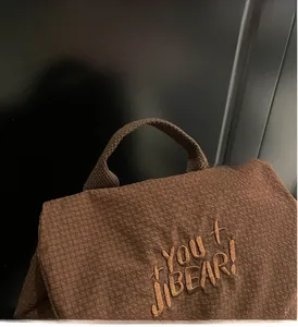 Close-up of brown pleated fabric backpack with YOU BEAR embroidery and sturdy handle
