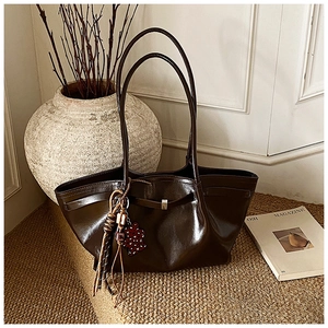 Detail of dark brown glossy leather tote bag with unique bead and tassel pendant