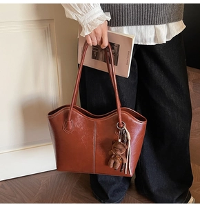 Close-up of brown oiled leather tote bag with plush bear charm and tassel detail